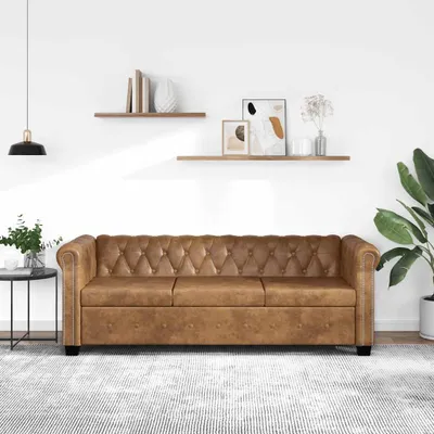A brown Chesterfield sofa is shown in a well-lit room with shelves on the wall and a plant in the corner.