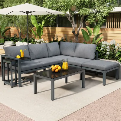 An outdoor patio scene featuring a gray sectional sofa set with a coffee table and side tables, decorated with oranges and drinks.