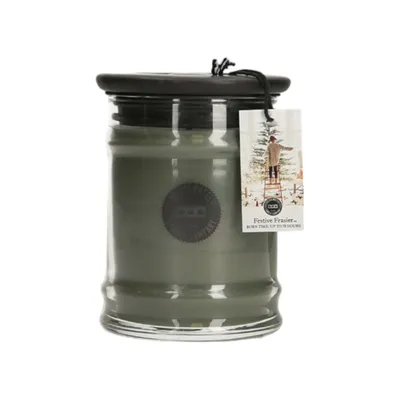 A green candle in a glass jar with a black lid and a decorative tag.