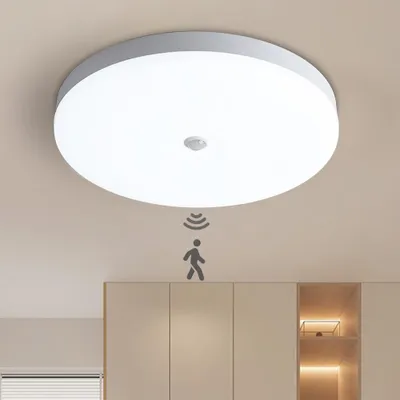 A white LED ceiling light with a motion sensor is mounted on a light-colored ceiling above a set of light-colored cabinets. A graphic of a person with motion waves is shown below the light, indicating its motion-sensing feature.