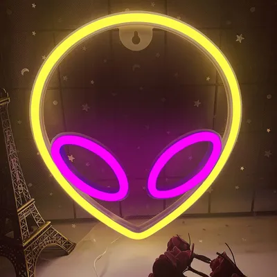 A neon alien head sign is displayed against a dark, star-speckled background, with a miniature Eiffel Tower and some roses in the foreground.
