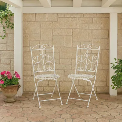 Two white metal chairs on a stone patio in front of a stone wall.