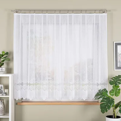 A white lace curtain hangs in a window, with a wooden windowsill visible below. A white shelf unit with decorative items is to the left, and a potted plant with large leaves is to the right.