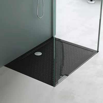 A black shower tray with a textured surface and a silver drain cover, set within a modern bathroom with glass shower walls and a grey wall.