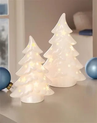 Two illuminated ceramic Christmas trees on a shelf, with blue ornaments in the foreground.
