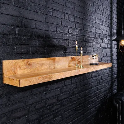 A wooden shelf mounted on a black brick wall, decorated with two candle holders and a glass dome with a bottle inside.