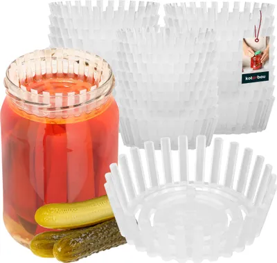 A glass jar filled with red pickled items and two pickles in front of it, surrounded by stacks of white plastic fermentation weights.