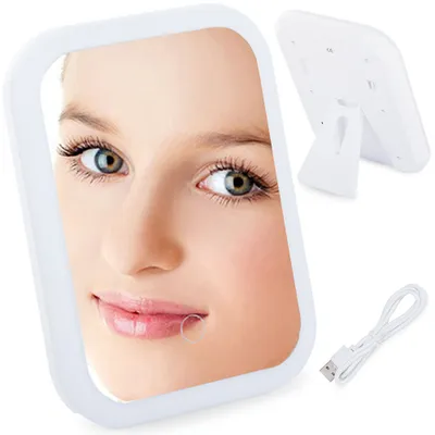 A close-up of a woman's face reflected in a cosmetic mirror, with the back of the mirror and a USB cable visible in the background.