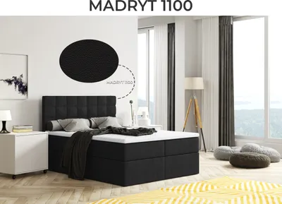 A bedroom scene featuring a black boxspring bed with a headboard, pillows, and a blanket. The room has large windows with curtains, a floor lamp, a nightstand with a lamp, and floor cushions. A yellow rug is visible in the foreground.