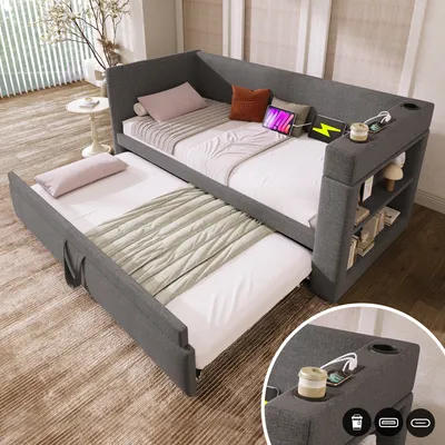 A grey upholstered daybed with a pull-out trundle bed, set up in a room with natural light and decorative elements.