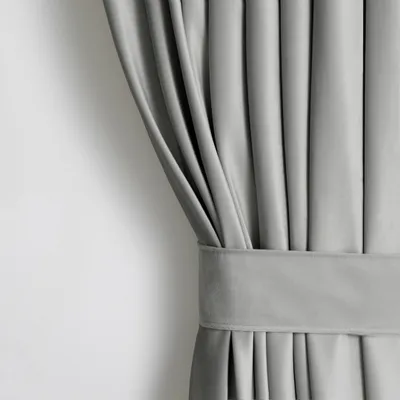 A close-up view of a silver velvet curtain, tied back with a fabric band.