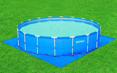 A round blue swimming pool filled with water, placed on a blue ground cloth on a green lawn.
