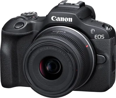 A black Canon EOS R100 camera with a kit lens is shown against a white background.