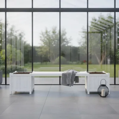 A white wooden bench with two integrated planters sits on a tiled patio in front of a large glass wall overlooking a garden.
