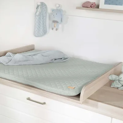 A baby changing mat with a blanket on it, placed on top of a dresser.