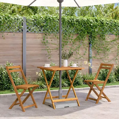 An outdoor patio scene with a wooden folding table and chairs set up under a large umbrella, with a wooden fence and greenery in the background.