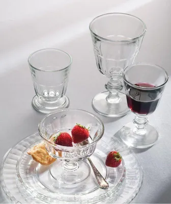 A collection of glassware, including wine glasses and small bowls, arranged on a white surface. Some glasses contain strawberries and a cracker.