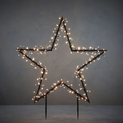 A lit star-shaped garden stake against a grey background.