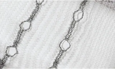 A close-up view of a white fabric with a gray mesh-like material laid on top, forming a pattern of interconnected loops.