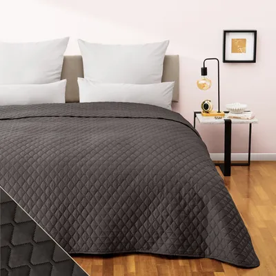 A dark gray quilted bedspread is laid out on a bed with white pillows.