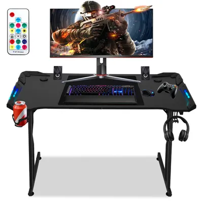 A gaming desk setup with a monitor, keyboard, mouse, controller, headphones, and a drink.