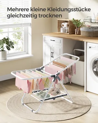 A small, foldable drying rack with clothes and shoes is placed on a rug in a laundry room setting.