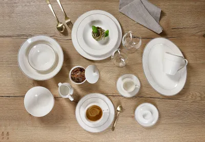 A collection of white porcelain dinnerware with gold trim, arranged on a wooden table.