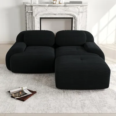 A black sectional sofa is shown in a well-lit room with a fireplace in the background and a rug on the floor.
