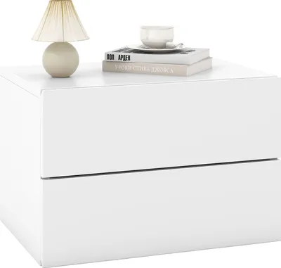 A white nightstand with two drawers, a lamp, and books on top.