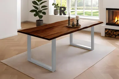 A wooden dining table with a live edge is set in a modern dining room with a fireplace and large windows.