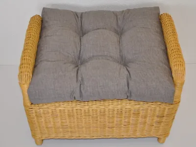 A close-up view of a wicker ottoman with a gray cushion.