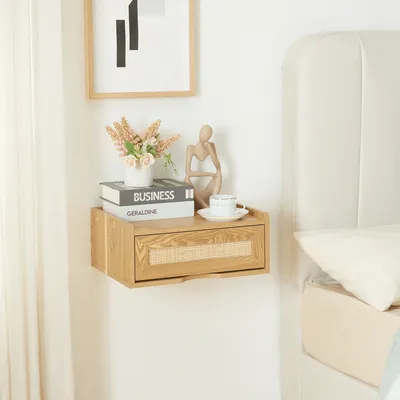 A wooden floating nightstand with a cane drawer front is mounted on a white wall next to a bed. It is decorated with books, a vase of flowers, and a decorative figurine.