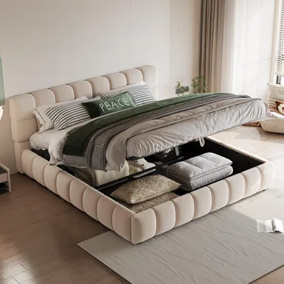 A beige upholstered bed with its storage compartment open, revealing stored items inside. The bed is made up with pillows and a green throw blanket.