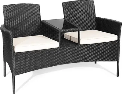 A black polyrattan garden bench with white cushions and a glass-topped table in the center.
