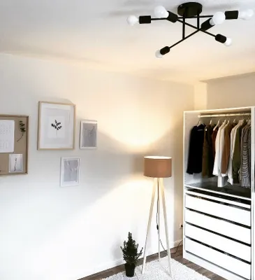 A room with a closet, floor lamp, and framed pictures on the wall.