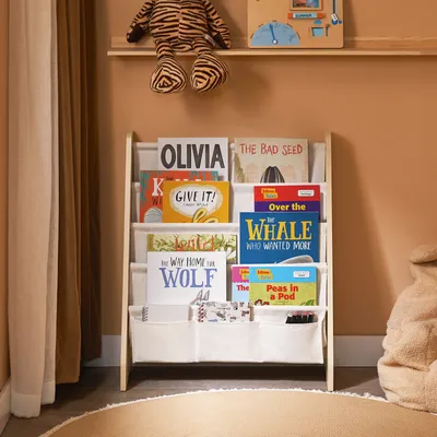 A children's bookshelf filled with books, placed in a room with a curtain and a beanbag chair.