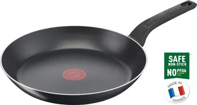 A black frying pan with a red heat indicator in the center, set against a white background. To the right, there are marketing badges indicating 'SAFE NON-STICK NO PFOA' and 'MADE IN FRANCE' with a French flag.