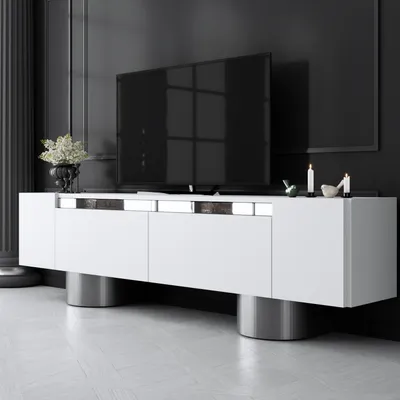 A modern white media console with metal cylinder legs is shown in a dark room.