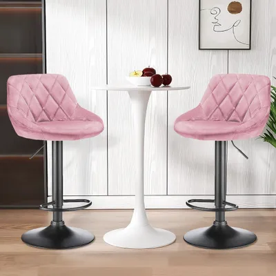 Two pink velvet bar stools are placed around a white tulip-style table, with a framed abstract artwork on the wall behind.