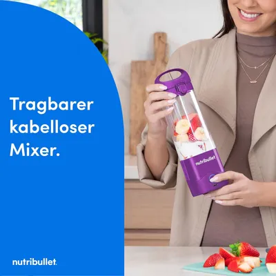 A woman holding a portable blender with fruits inside.