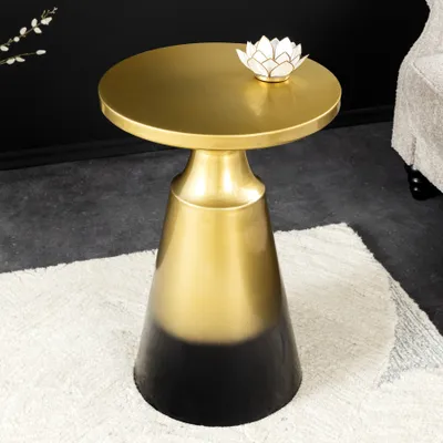 A gold and black ombre side table with a decorative lotus flower on top, placed on a rug in a room.