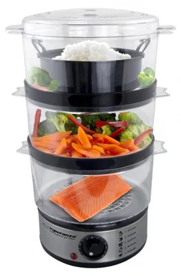A multi-tiered electric food steamer filled with food, including salmon, carrots, broccoli, and rice. The steamer has a silver base with a black control dial and indicator lights.