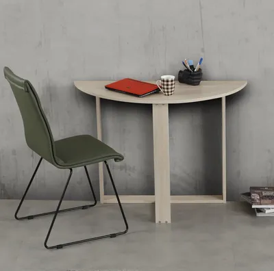 A green chair sits next to a light wood desk with a laptop and mug on it.