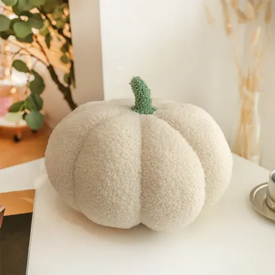 A white, fluffy pumpkin-shaped pillow with a green stem sits on a white table.