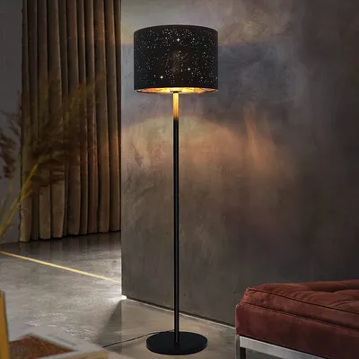 A floor lamp with a star-patterned shade is placed in a room with curtains and a textured wall.