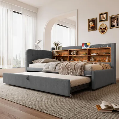 A grey upholstered daybed with a pull-out trundle bed is shown in a bedroom setting.