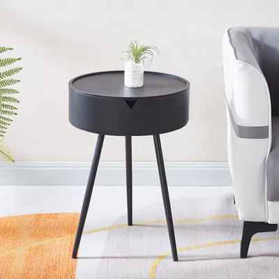 A minimalist black side table with a small plant on top, placed next to a sofa in a living room setting.