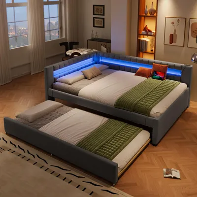A modern bedroom with a grey upholstered bed frame featuring integrated blue LED lighting, a pull-out trundle bed, and decorative pillows and blankets.