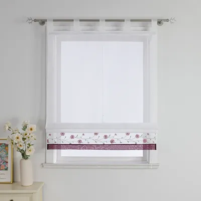 A white wall with a window covered by white sheer curtains and a decorative roman shade with a floral pattern.