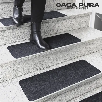 A person wearing black boots walks down a set of stairs with dark gray stair mats.